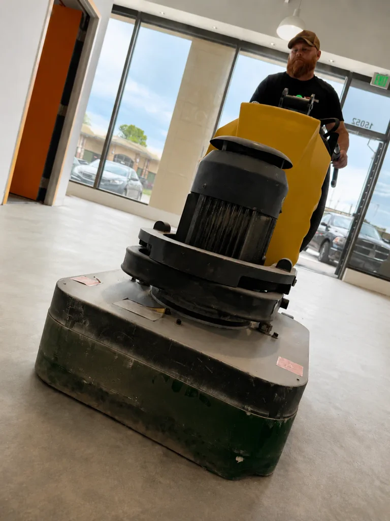 Crew member running an industrial floor grinder to prep concrete for epoxy